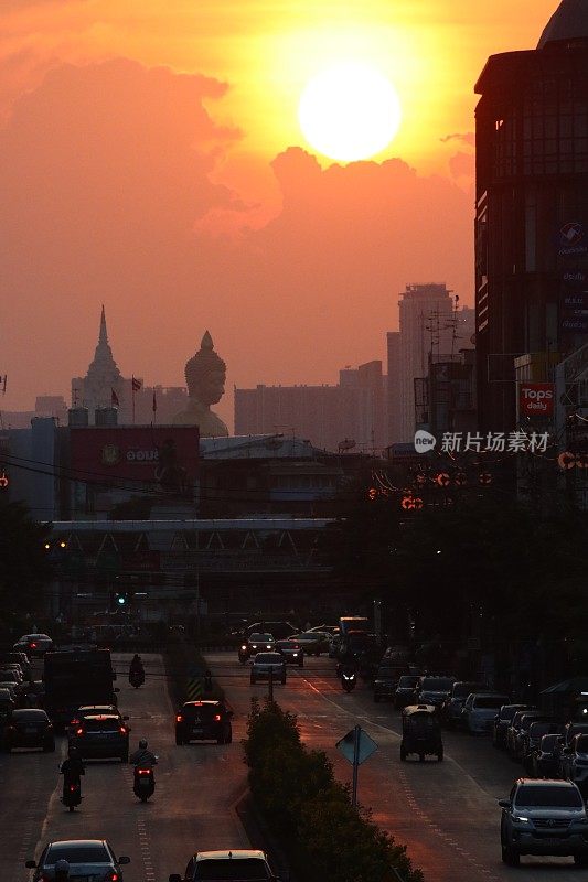 橙色的夕阳天空在佛祖Dhammakaya Thep Mongkol(青铜雕像)和Wat Paknam Bhasicharoen(皇家寺庙)之上，从立交桥上看高速公路上的交通堵塞，摩托车，汽车，空气污染，烟雾，汽车烟雾，重点在前景